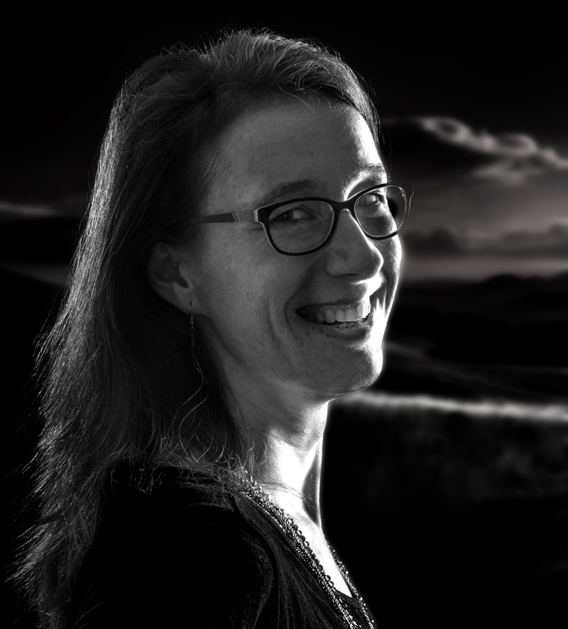 Susann Prüß, lächelnd im Profil, vor einem dunklen Landschaftshintergrund – Porträtaufnahme in Schwarz-Weiß