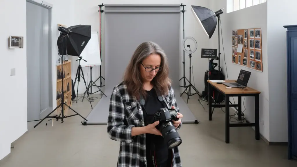 Susann Prüß prüft die Kamera im Fotostudio vor grauem Hintergrund; Softboxen und Set im Freiraum in Glückstadt.