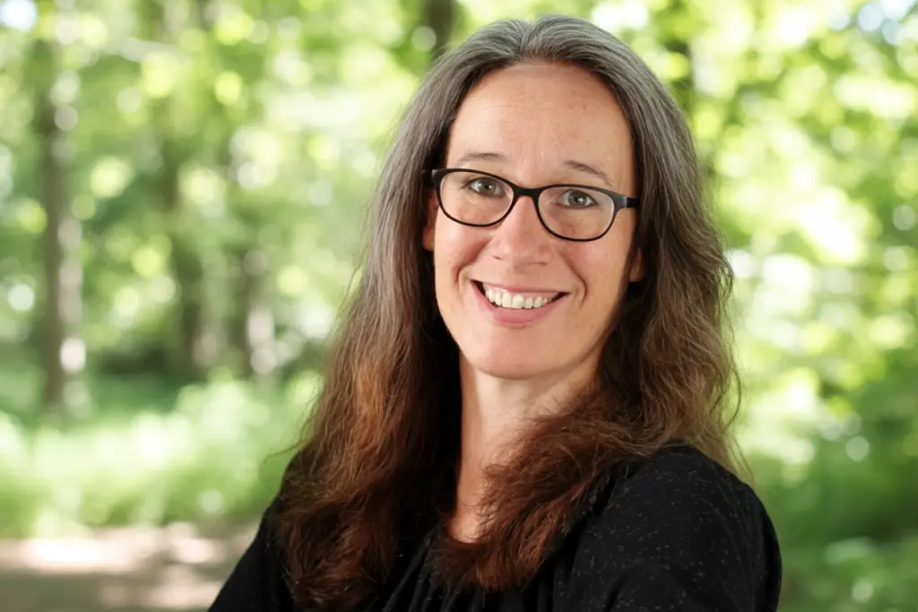 Porträt von Susann Prüß im Grünen, lächelnd mit Brille – Mediengestalterin/Webdesign.