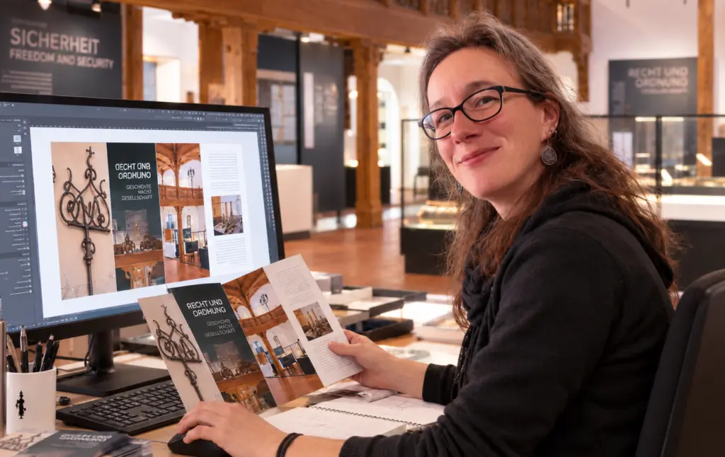 Susann Prüß gestaltet eine Broschüre für das Dithmarscher Landesmuseum am Computer und prüft das gedruckte Layout.