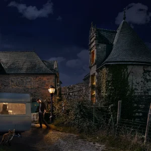 Nächtliche Szene: Ein kleiner Caravan steht vor einem alten Haus, eine Laterne erhellt den Weg, ein Mann geht zum Wohnwagen und ein Fuchs schleicht im Vordergrund; im Hintergrund ein großer Vollmond und beleuchtete Fenster im alten Haus